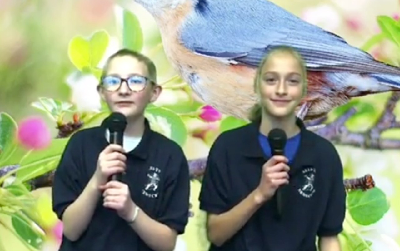 Two students from News Crew holding microphones on camera.